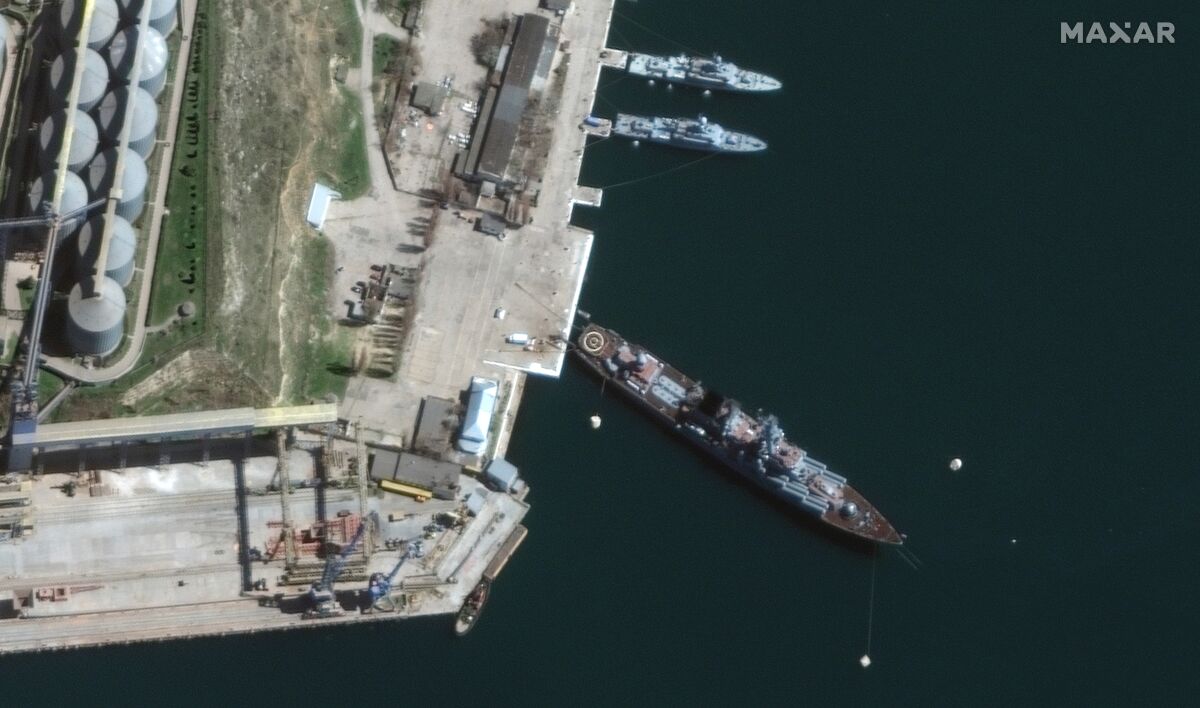 An aerial view of a ship sitting at an angle in port near two smaller ships