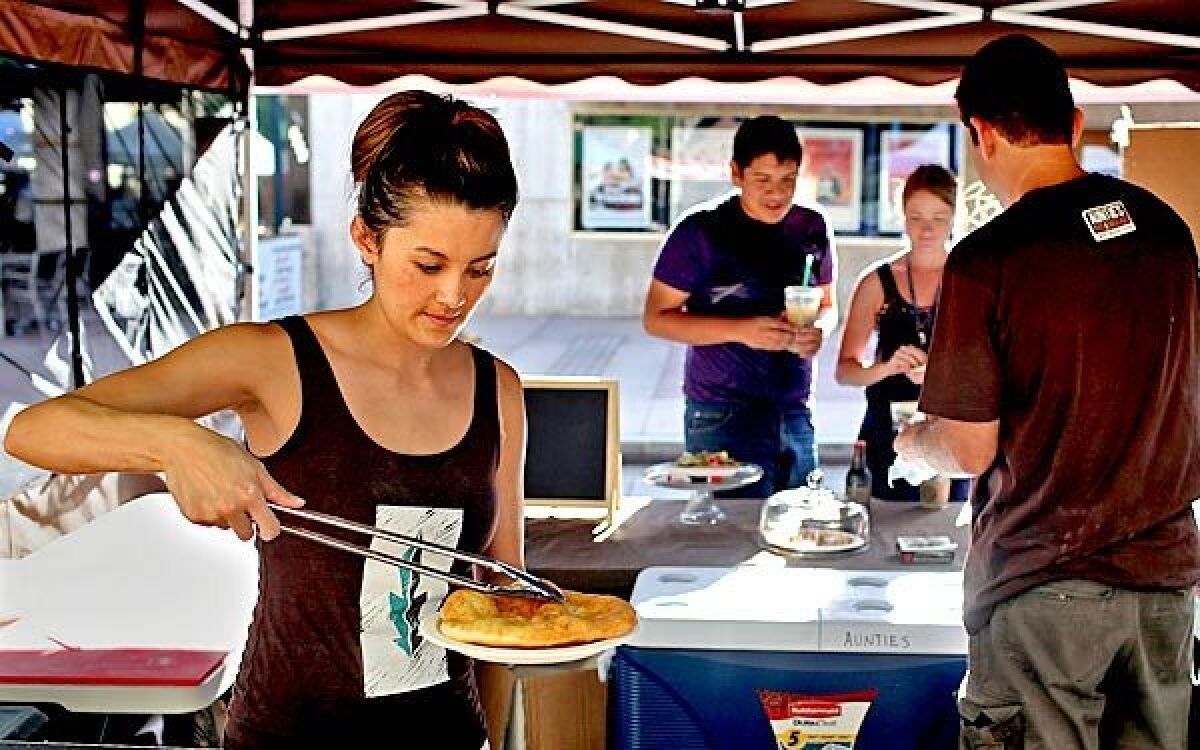 Kate Koyama, co-owner of Auntie's Native American Fry Bread, prepares a fry-bread taco as co-owner Eric Evans, right, talks to customers at their stand at Wednesday's Westwood Farmers Market.