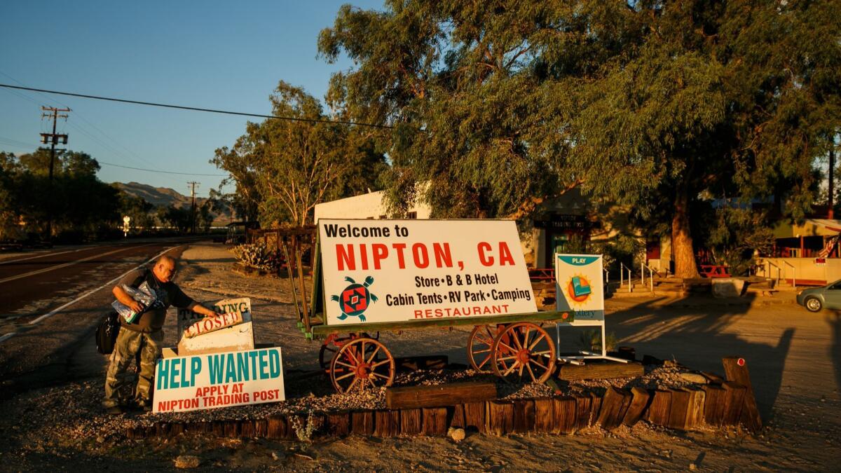 A man tends to signs beside a road leading into Nipton, Calif., in August 2017.