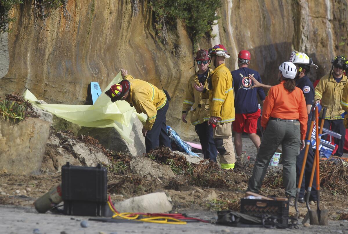 A fire captain looks under a tarp where a section of oceanfront bluff collapsed at Grandview Beach in Encinitas, killing three members of one family.