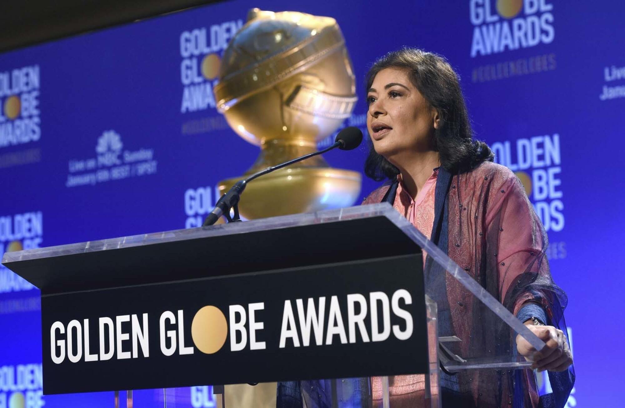 A woman speaks at a lectern with the words Golden Globe Awards on it in front of a replica of the award statuette