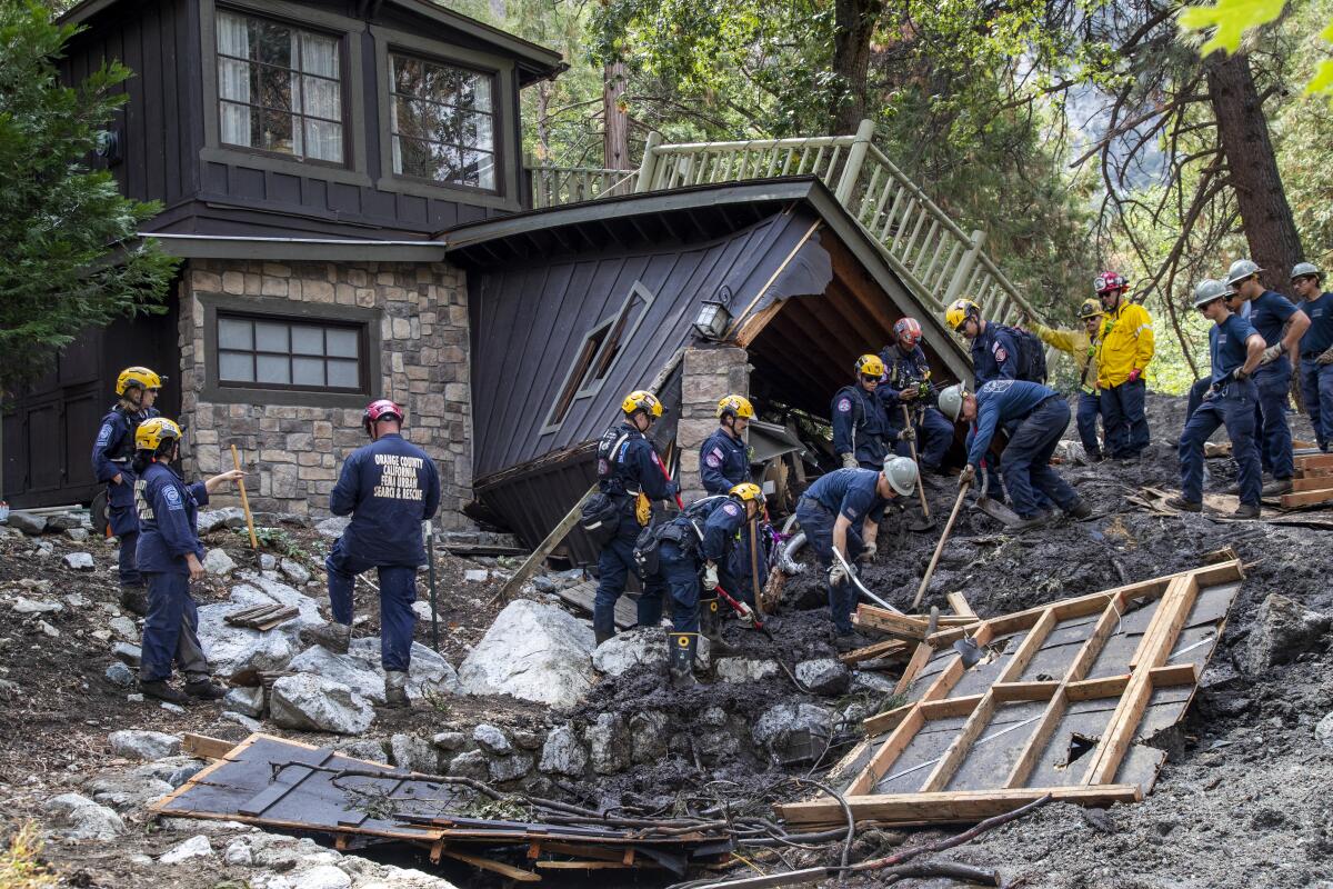 Search and rescue crews in helmets work outside a destroyed home surrounded by mud and debris