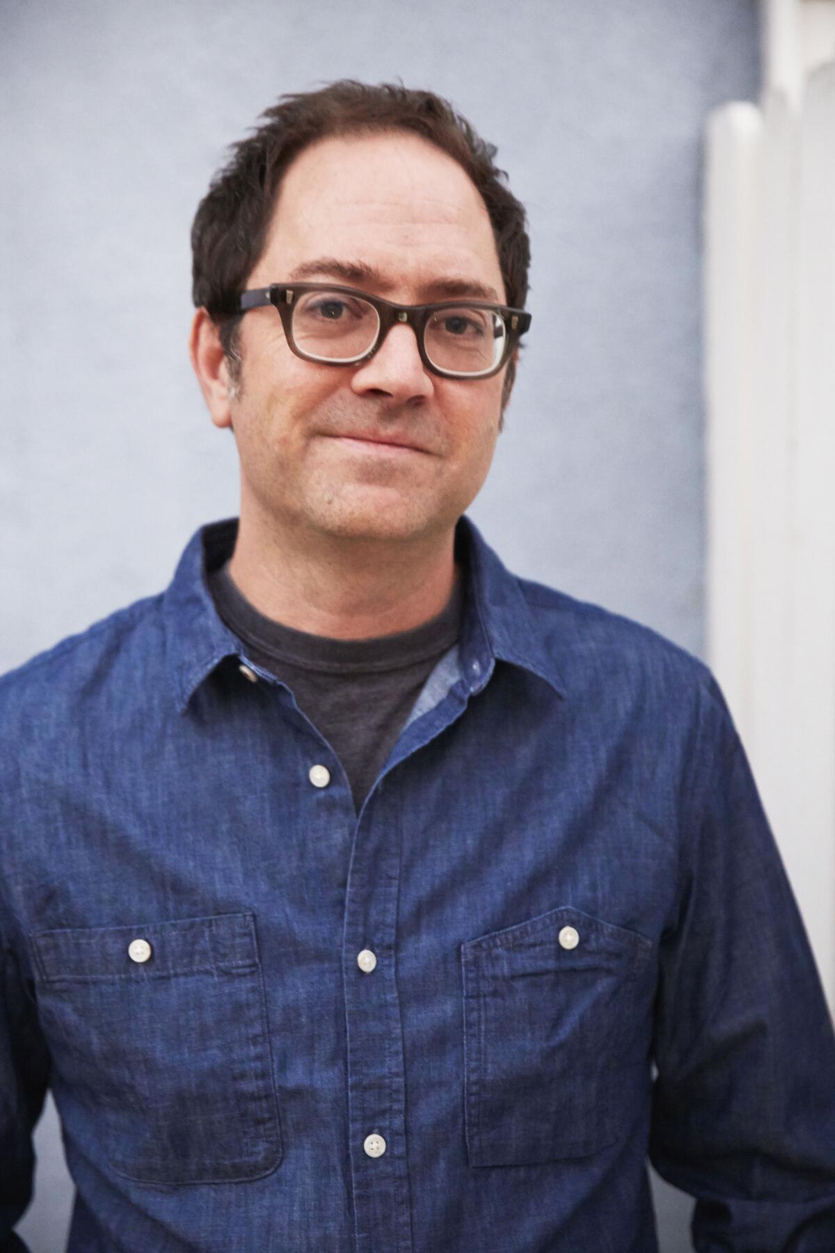 A portrait of a man wearing glasses and a dark blue shirt.