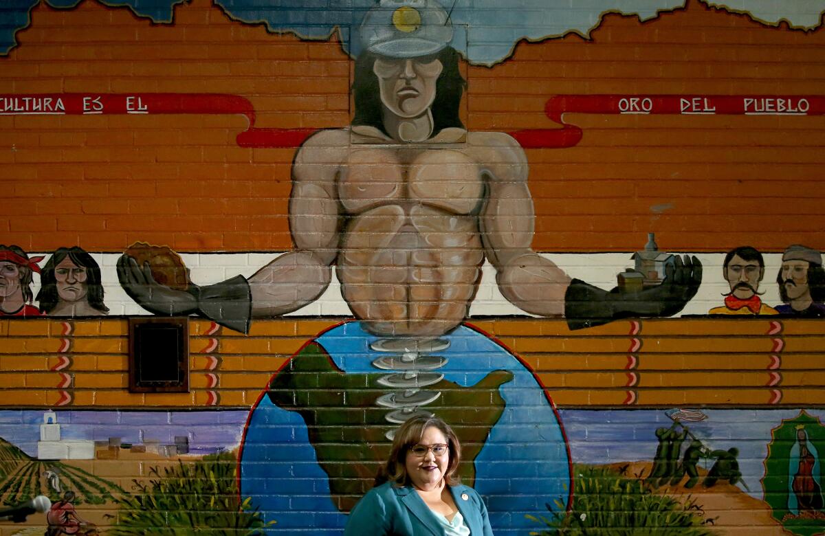 A woman stands in front of a painted mural. 