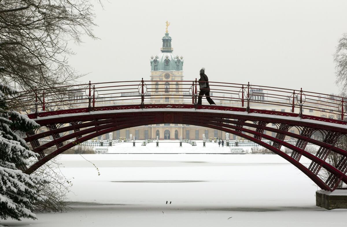A snowy scene of Charlottenburg Palace in Berlin with a person crossing a bridge in foreground
