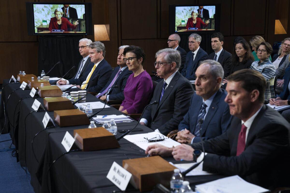 Sen. Elizabeth Warren, D-Mass., on a screen in the background, questions witnesses during a hearing