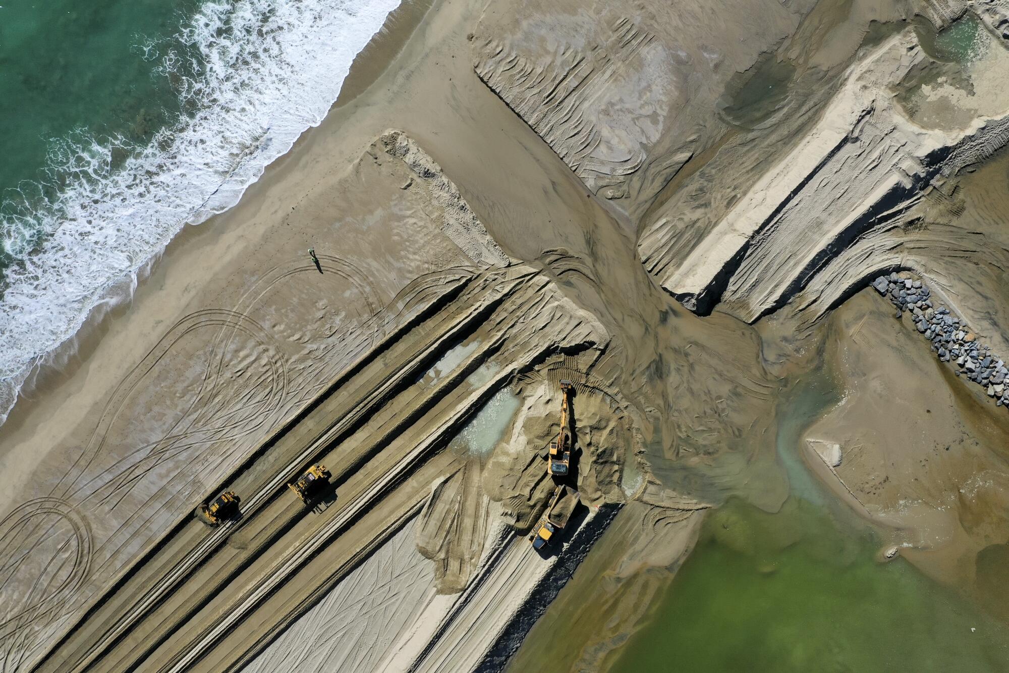An aerial view of heavy machinery opening up the Santa Ana river sand berm to allow ocean water back in the Santa Ana River 