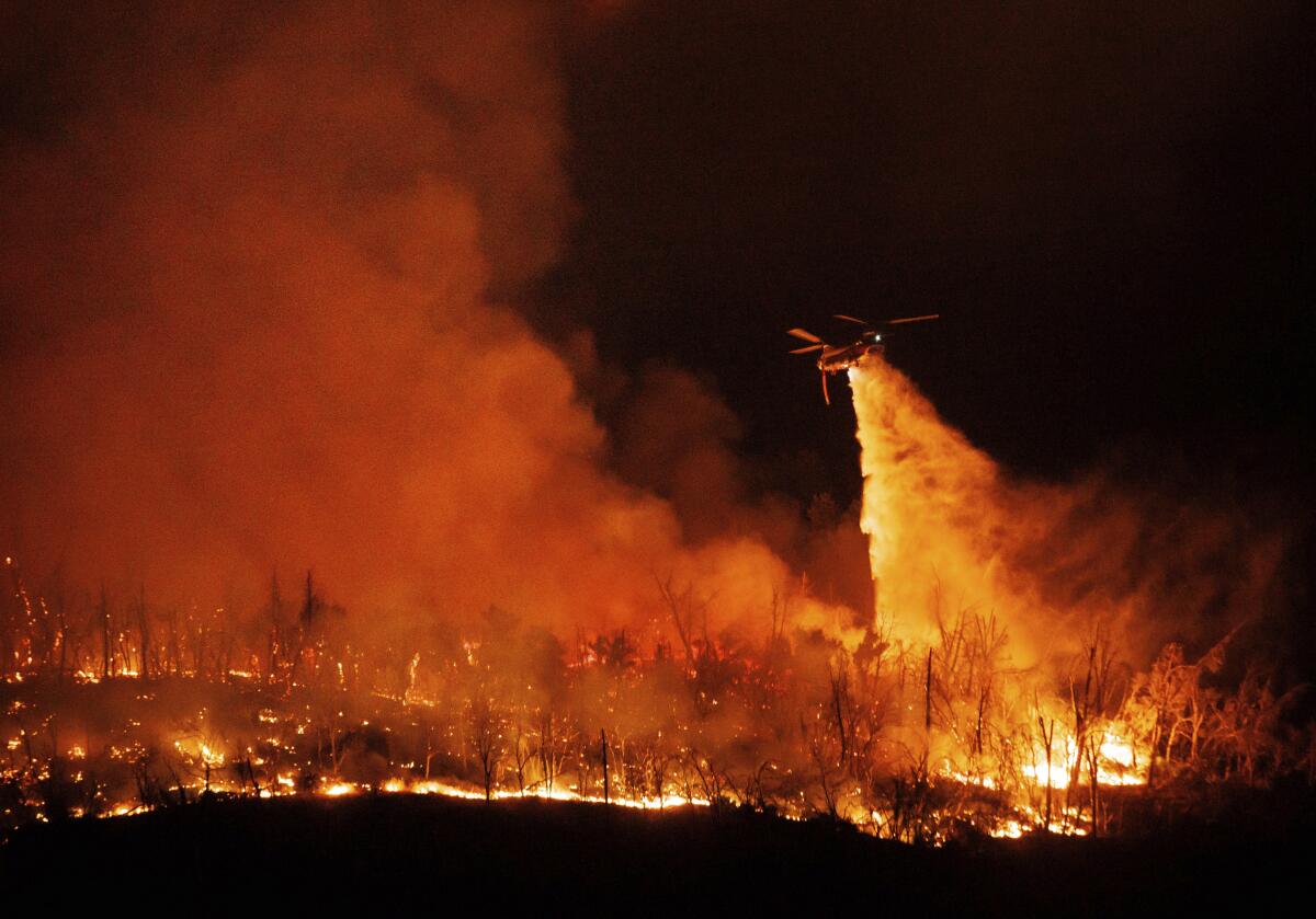 A night-flying helicopter drops water on flames.
