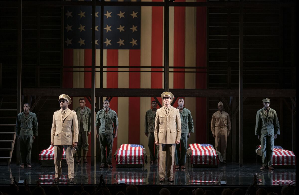 A cast of actors, clad in soldier's uniforms, onstage.