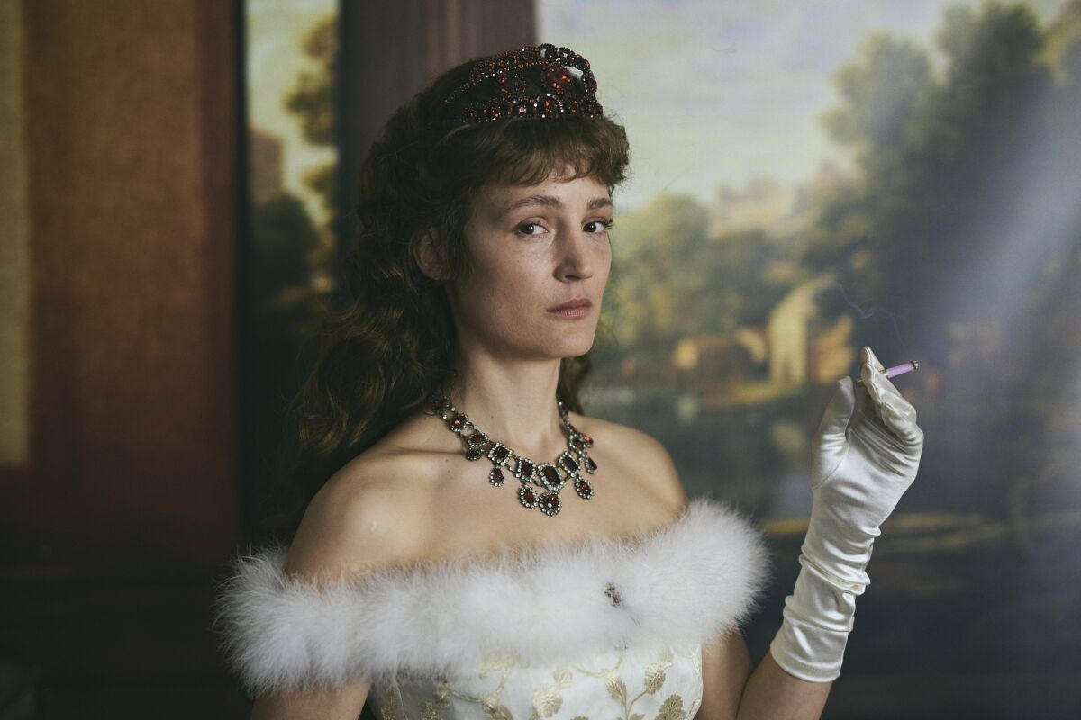 A woman in Victorian evening dress smokes a cigarette in the movie 'Corsage.'