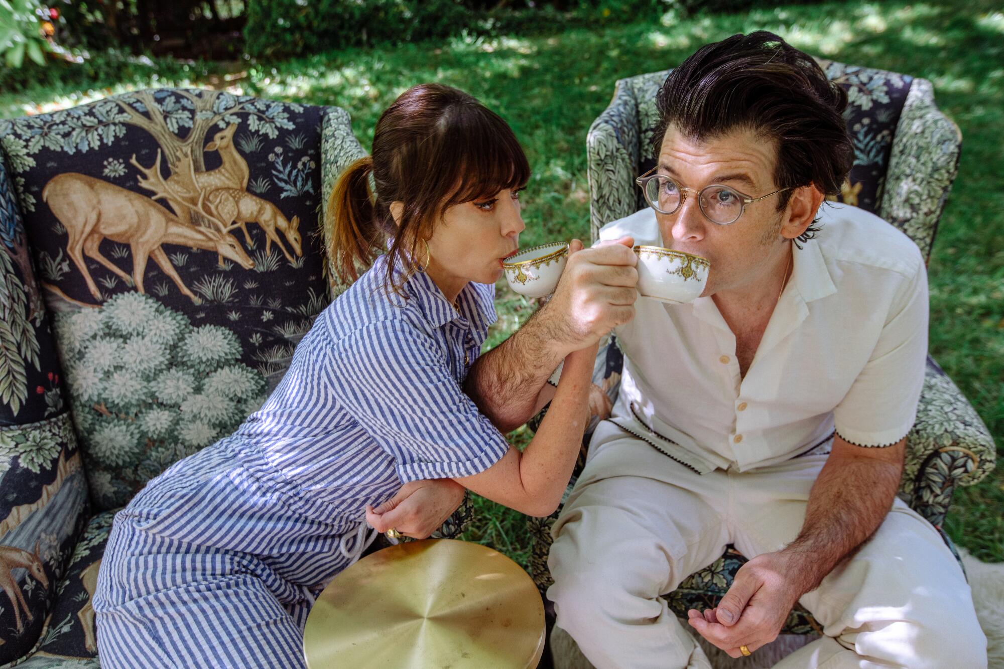 Natasha Leggero and Moshe Kasher entwine arms to drink from cups in their backyard in Los Angeles.