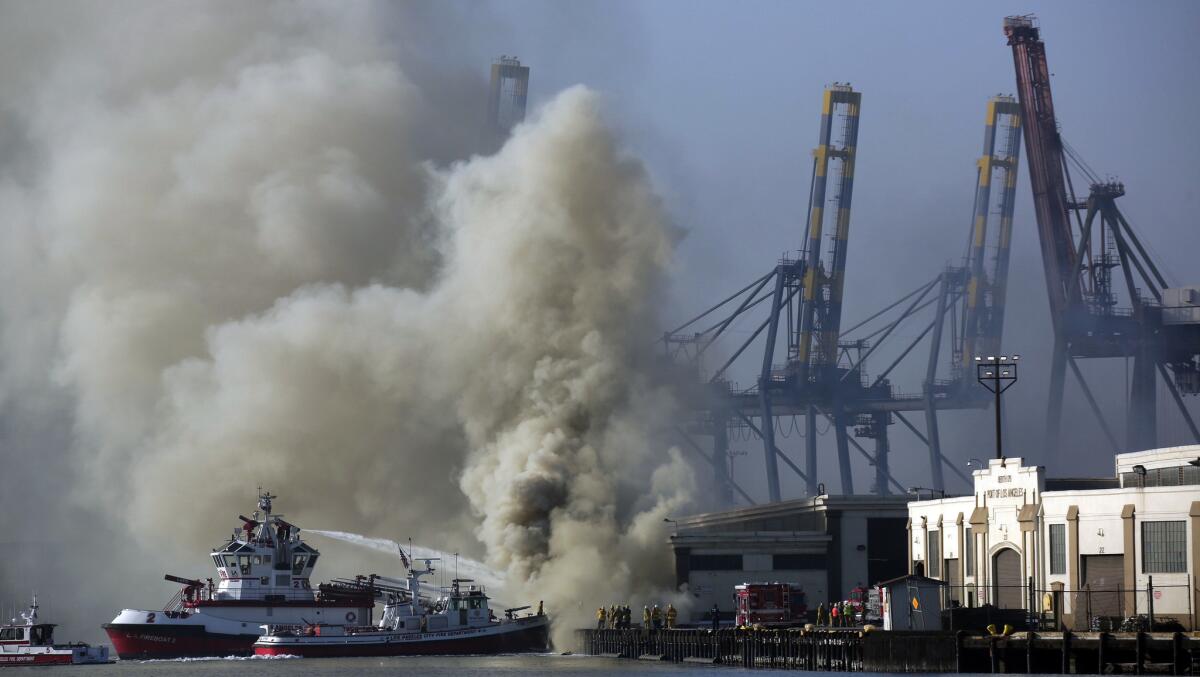 A plume rises from a stubborn fire at the Port of Los Angeles that continues to burn World War II-era lumber pylons soaked in creosote, prompting air quality concerns Tuesday.
