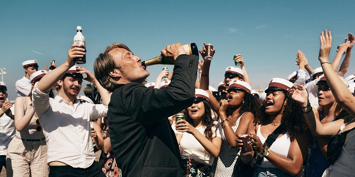 Mads Mikkelsen's character drinks from bottle in the midst of a crowd of celebrating students.