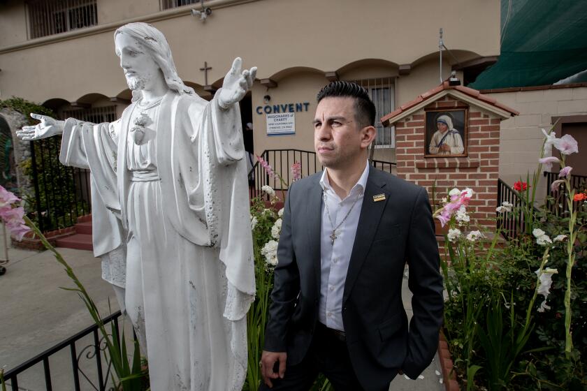 Lynwood, CA - June 14: Julian Del Real-Calleros, poses next to a statue of Jesus Christ and portrait of St. Teresa "Mother Teresa" of Calcutta at her Missionaries of Charity Queen of Peace Shelter, St. Emydius Church in Lynwood Wednesday, June 14, 2023. Real-Calleros is a Lynwood school trustee and one of LGBT Catholic Christians who are opposed to the Dodgers honoring the Sisters of Perpetual Indulgence on Pride Night. (Allen J. Schaben / Los Angeles Times)