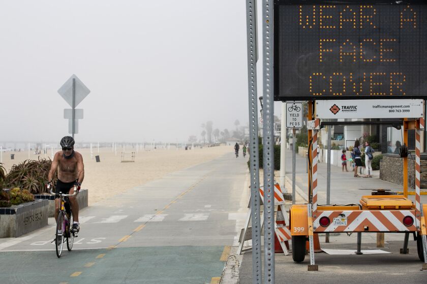 HERMOSA BEACH, CA - SEPTEMBER 04: A cyclist passes a sign advising beach goers to wear masks on Friday, Sept. 4, 2020 in Hermosa Beach, CA. (Josie Norris / Los Angeles Times)