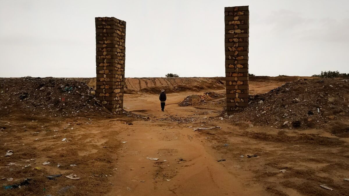 Chamseddine Marzoug passes through two brick columns that mark the entrance to the donated cemetery where he buries migrants, between olive groves and the town dump. He is trying to raise money to build a new cemetery.