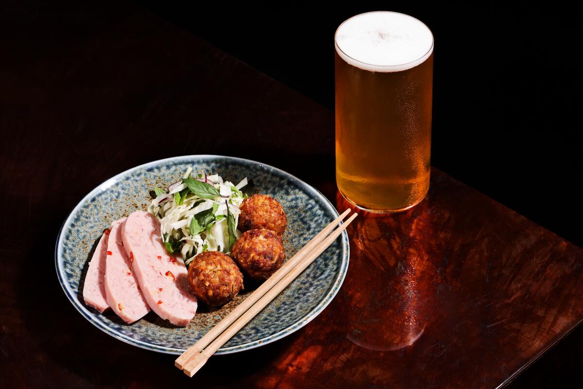 A dinner plate of naem, a Thai pork-loin sausage, with fried crispy rice balls and salad, next to a tall glass of beer