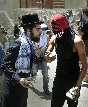 A member of Neturei Karta, a fringe of the ultra-Orthodox movement within the anti-Zionist bloc in Israel, talks with a masked Palestinian youth as he shows his support during clashes with Israeli police in the mostly Arab neighborhood of Silwan in Jerusalem. Palestinian protesters clashed with Israeli police as dozens of ultra-nationalist Jews carried Israeli flags through Silwan to assert Jewish sovereignty over all of Jerusalem, according to the organizers of the march.