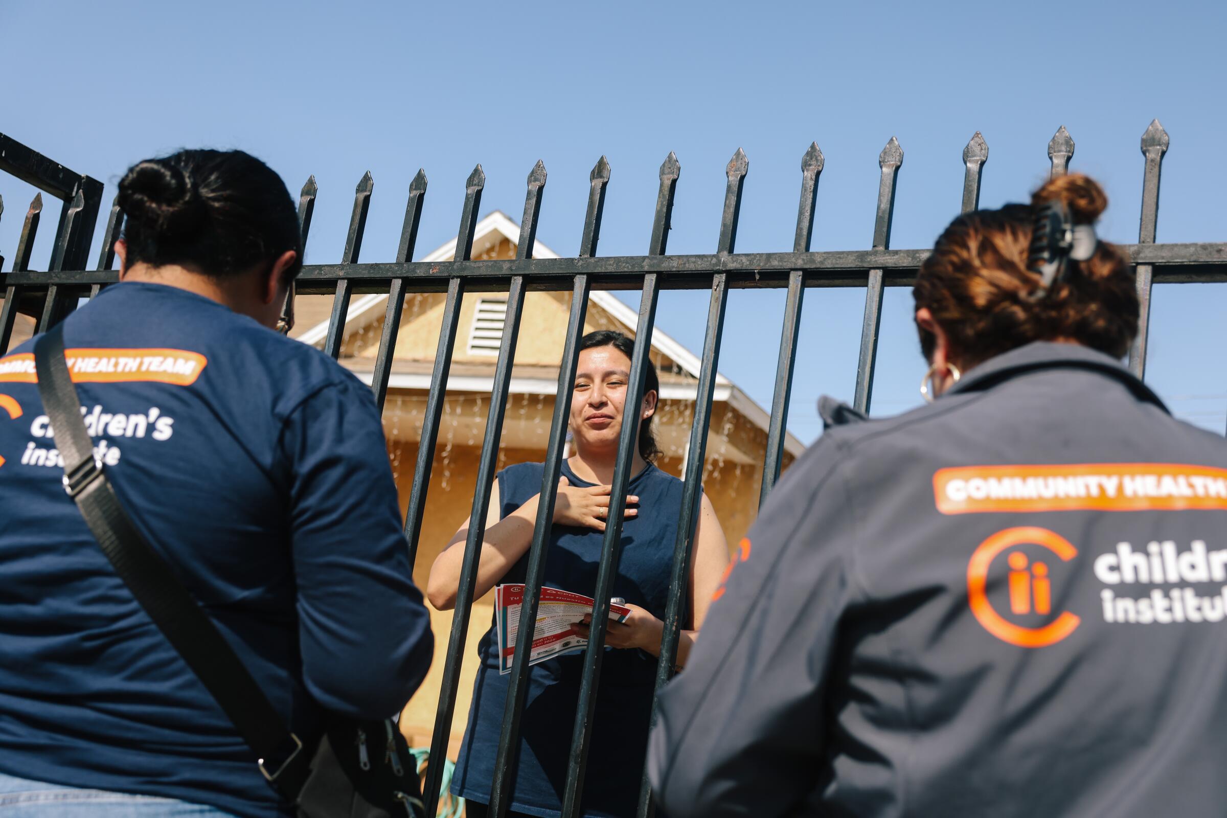 Maria Trujillo and Elizabeth Calvillo with Children's Institute speak with Brenda Montes, 26, through a fence in Watts.