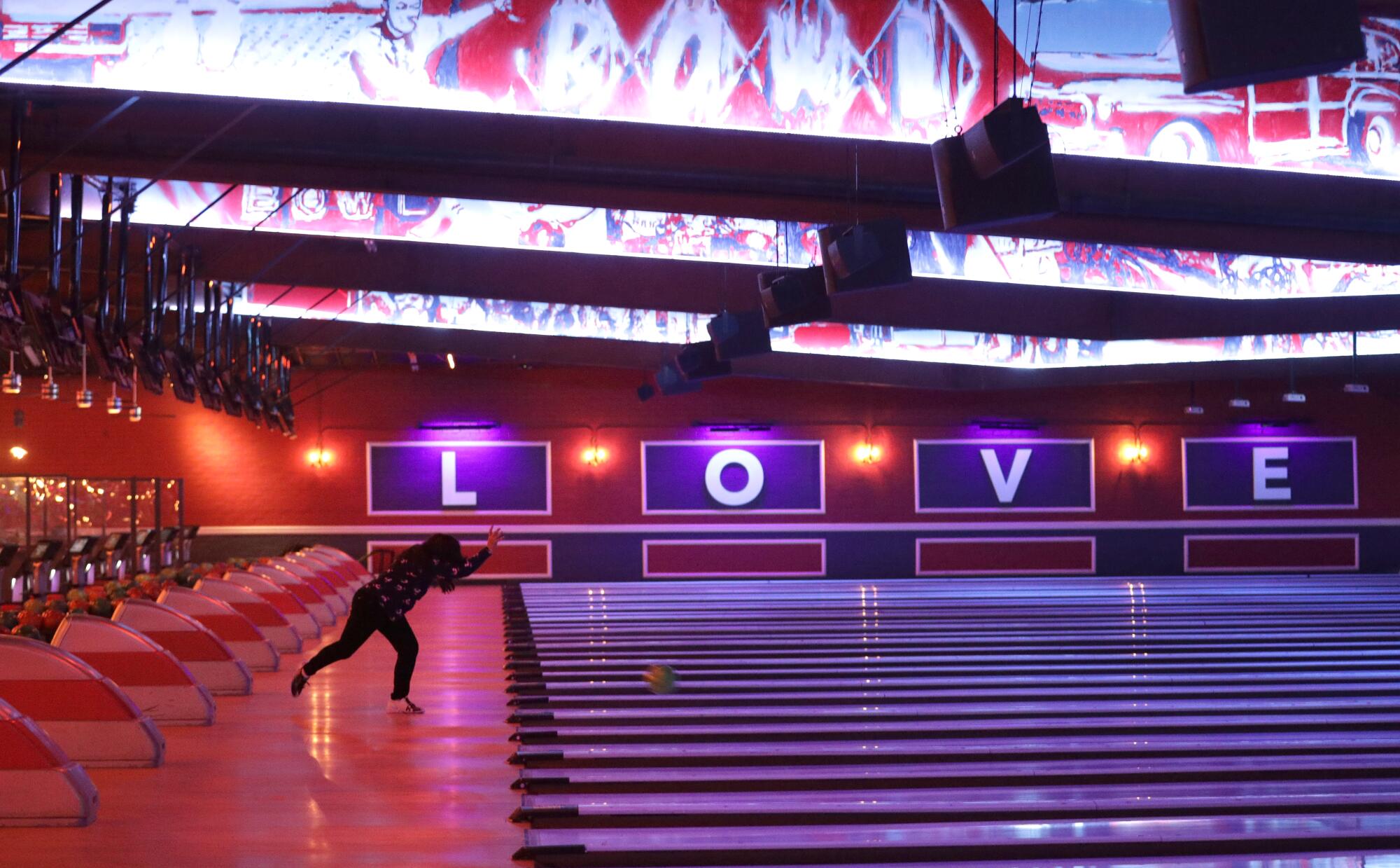 A woman bowls in a seemingly empty bowling alley