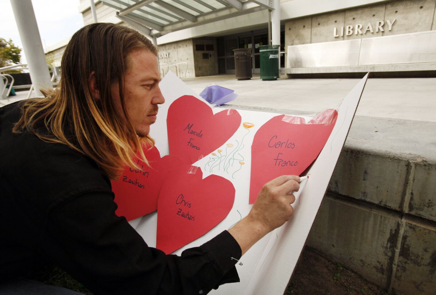 In front of the closed Santa Monica College library, Venice resident Nate Edelson makes a sign honoring the victims of Friday's deadly shooting rampage.