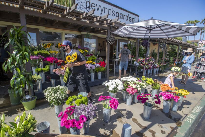 SEAL BEACH, CA -- FRIDAY, MAY 8, 2020: Empoyee Moy Ramirez, left, places flowers on display as Christina Dagle, right, and her daughter Eleanor Eades, 4, of Seal Beach, buy flowers for a friend from Devynn's Garden in Seal Beach, CA, on May 8, 2020. Some businesses are reopening under a relaxation of the state's stay at home order. Bookstores, music stores, toy stores, florists, sporting goods retailers, clothing stores and others can reopen for pickup and curbside service. (Allen J. Schaben / Los Angeles Times)