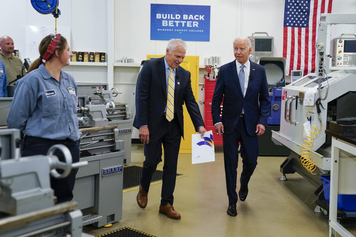 President Biden and another man walk past machine workers.