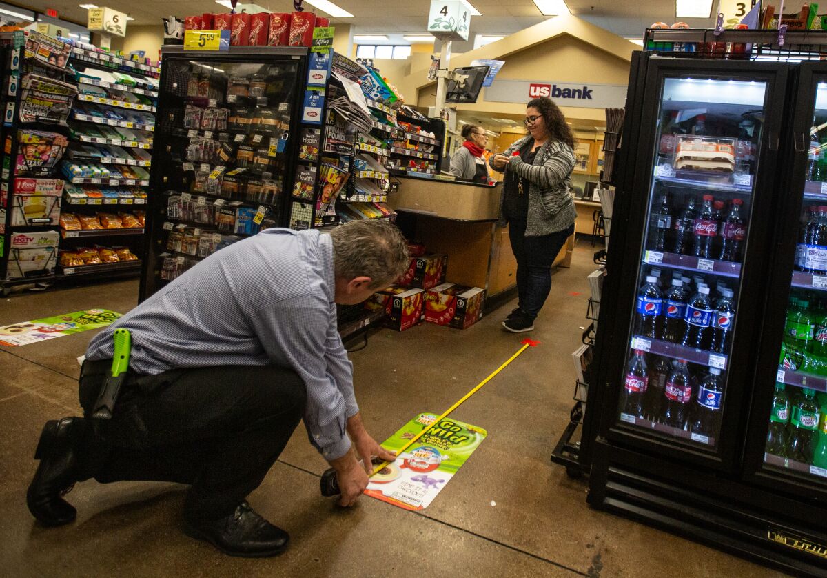 Workers at a Ralphs store in Westchester place marks on the floor to help customers observe social distancing guidelines