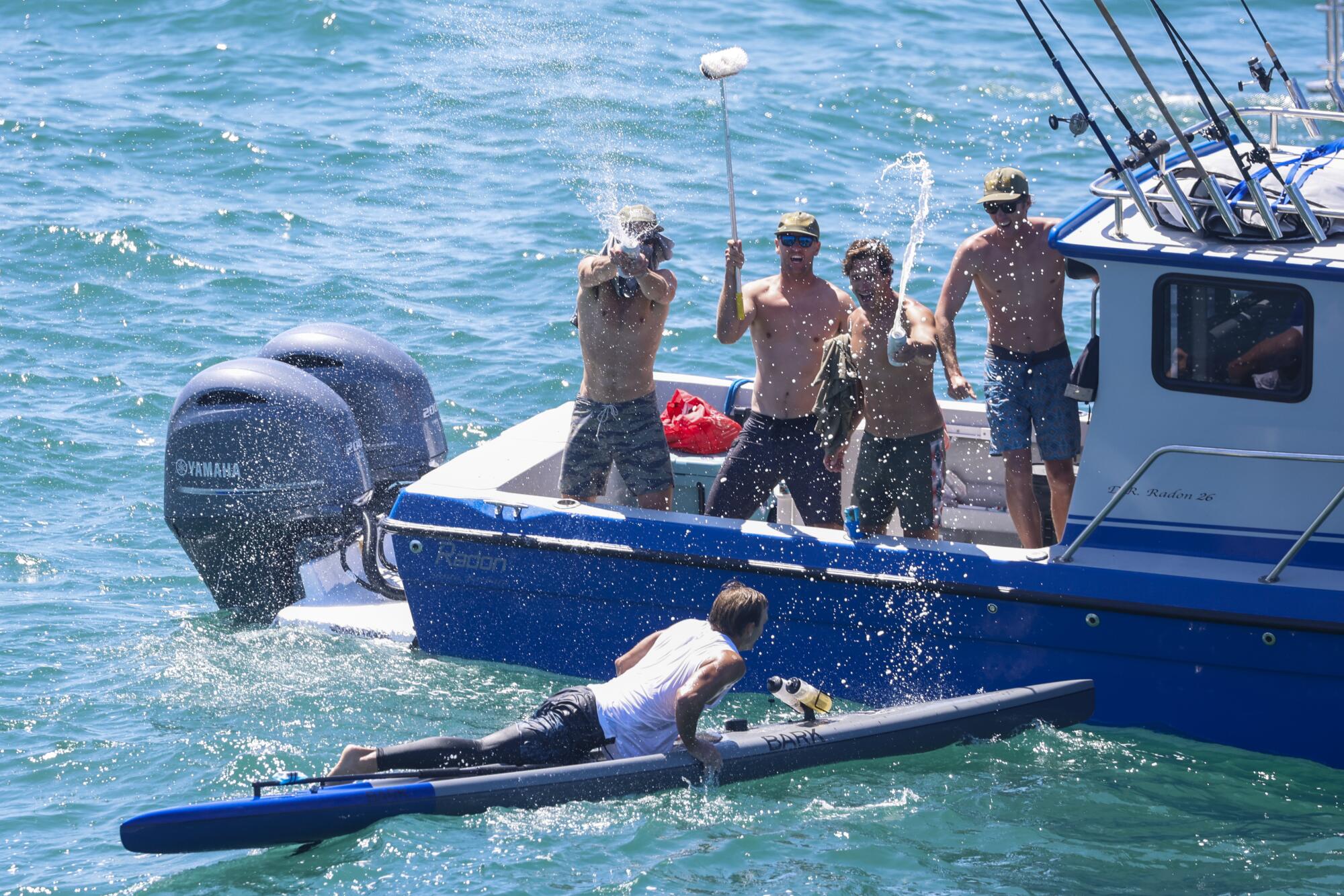 Jake Miller on his paddleboard, is congratulated by his team on a boat