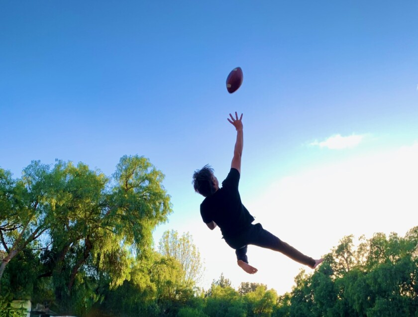 Tanner Prescott of Newbury Park leaps on his trampoline while trying to catch a football as part of his training session.