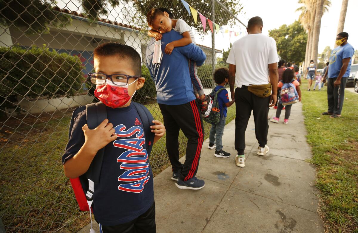 Students and parents wear masks in a line outside a school