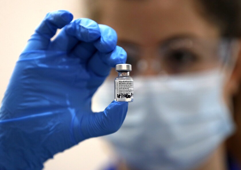 In a blue-gloved hand, a masked nurse holds a vial of the Pfizer-BioNTech COVID-19 vaccine.