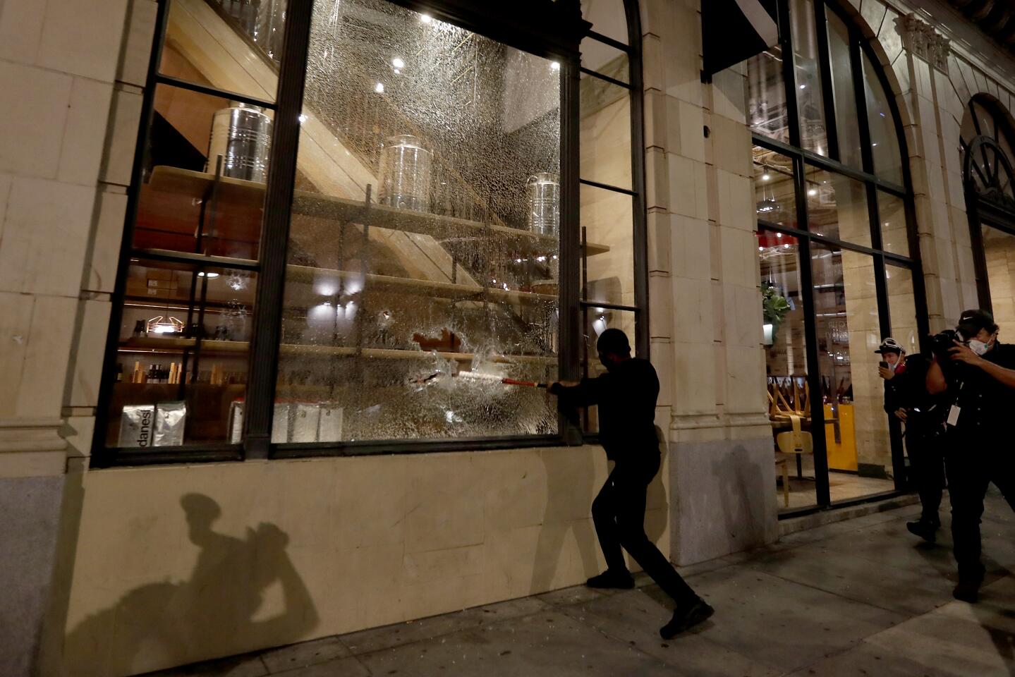 A man smashes the window of a business in downtown Los Angeles