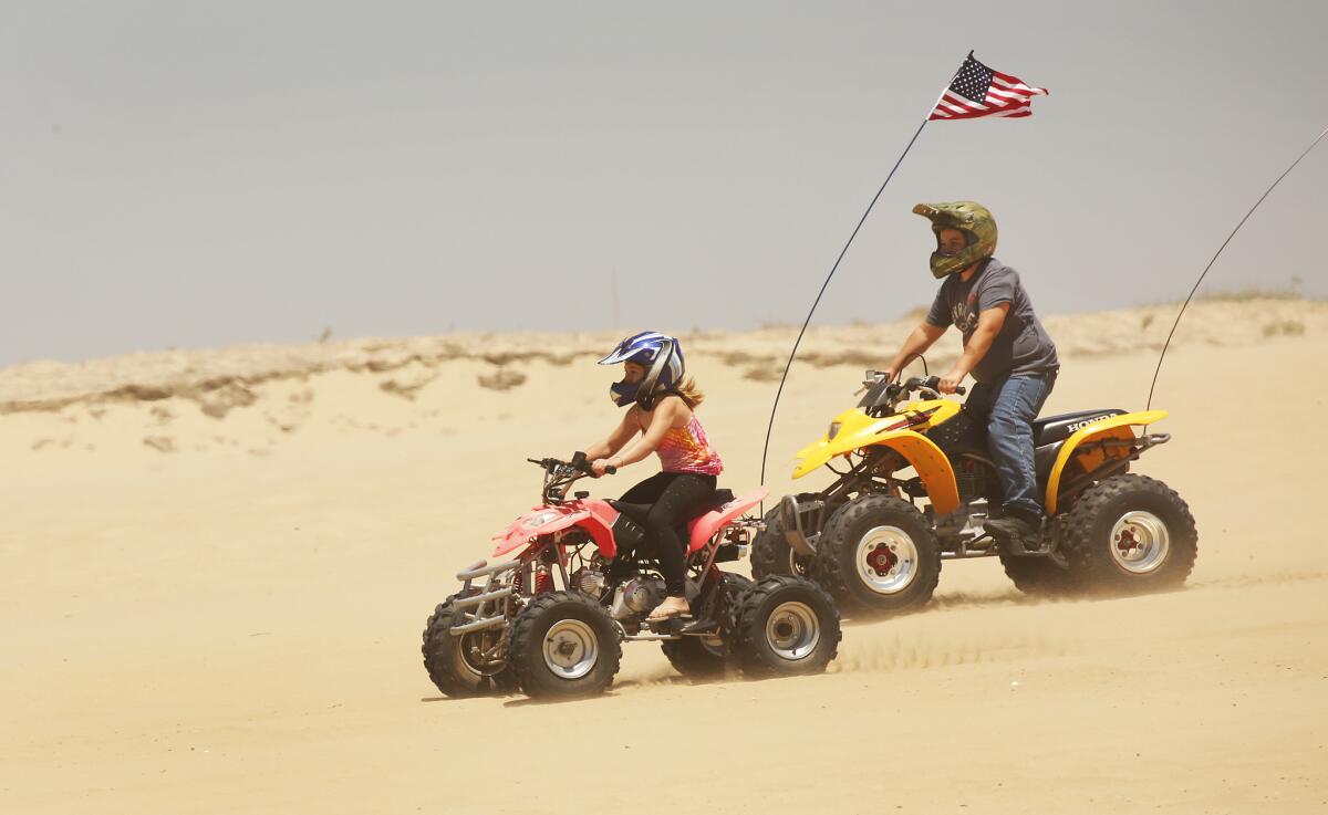 A girl and boy ride all-terain vehicles on a sand dune at Oceano Dunes 