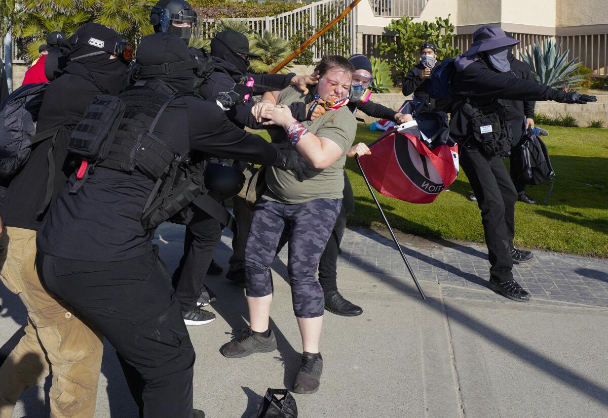 In this Jan. 9, 2021, photo, black-clad anti-fascist counterprotesters fight a person on the Pacific Beach boardwalk.