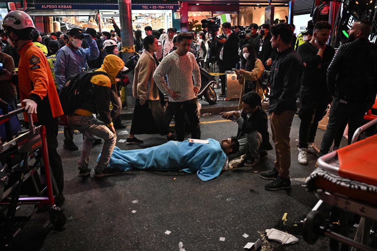A man lies under a blanket in a crowded street.