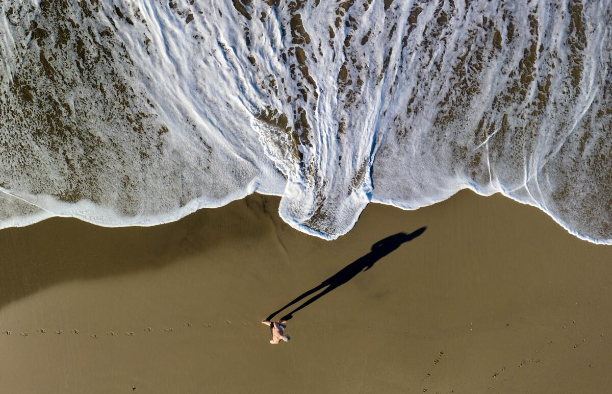 A man casts a long shadow as he jogs along the surf line in Santa Monica, CA. 