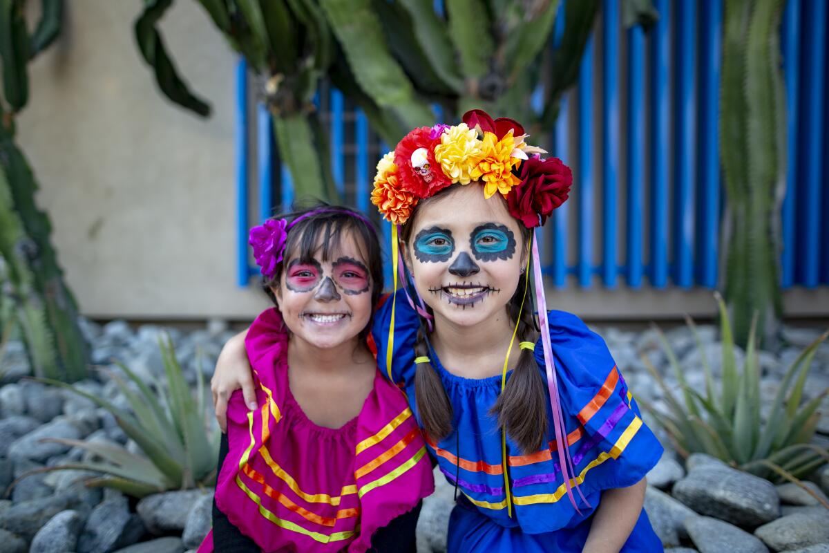 Two children with calavera face paint, flower headpieces and traditional dresses. 