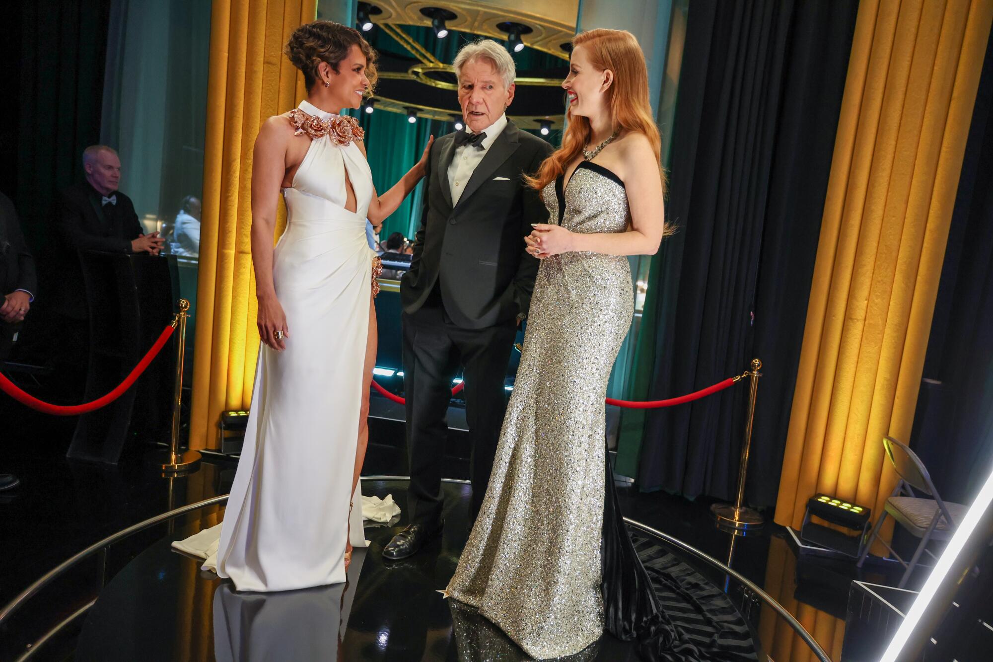Two women in evening gowns flank a man in a tux  backstage at the Oscars.
