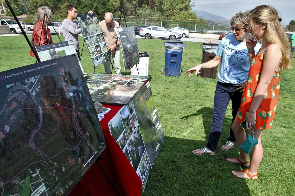 Flintridge Sacred Heart Academy teacher and event organizer Leslie Miller, right, talks with former student Brikk Bralley while they look at maps of the area to be saved at the school's Cottonwood Arts & Eco Festival at Memorial Park in La Cañada Flintridge on Friday, June 5, 2015.