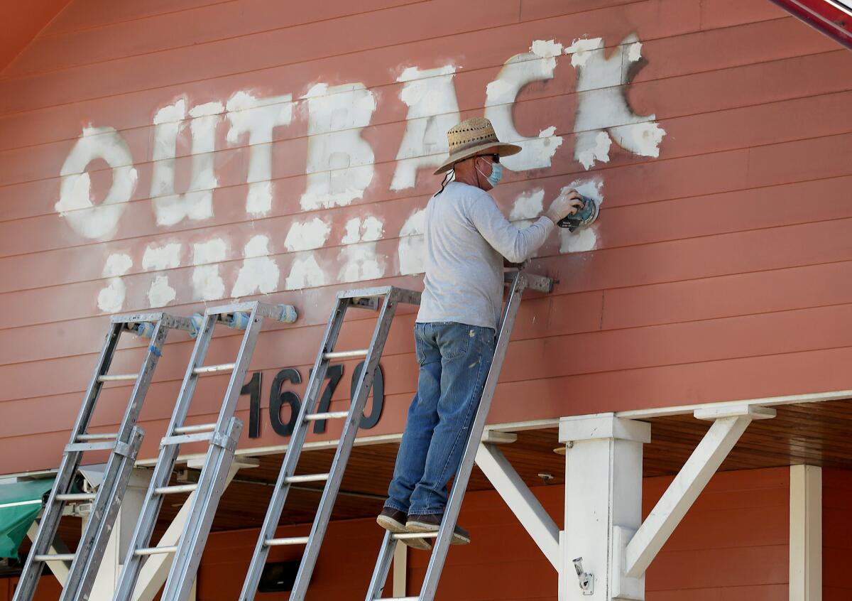 A worker sands away the last remnants of an Outback Steakhouse at 1670 Newport Blvd., in Costa Mesa