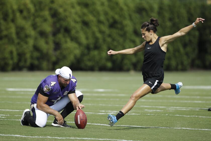 Baltimore Ravens' Sam Koch holds the ball for United States soccer player Carli Lloyd as she attempts to kick a field goal after the Philadelphia Eagles and the Baltimore Ravens held a joint NFL football practice in Philadelphia, Tuesday, Aug. 20, 2019. (AP Photo/Matt Rourke)