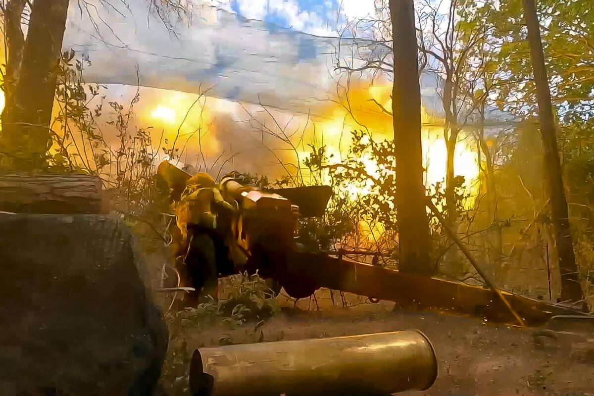 Russian soldiers fire a 152-mm howitzer from amid trees.