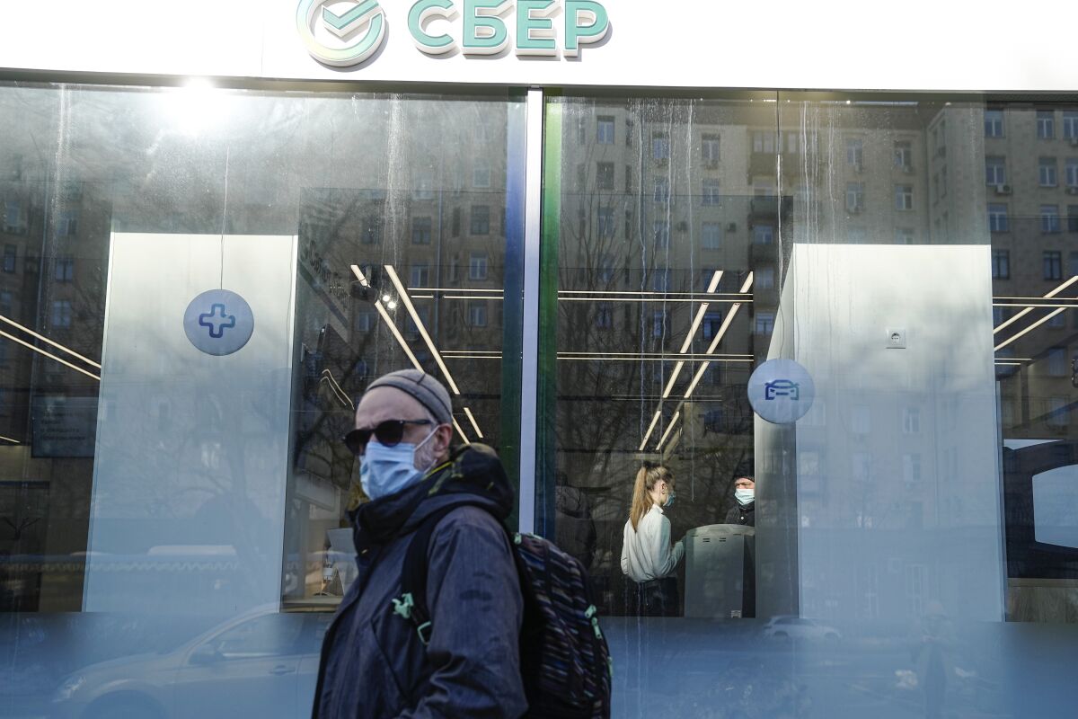 A man walks past an office of Sberbank in Moscow, Russia, Wednesday, March 2, 2022. Ordinary Russians are facing the prospect of higher prices as Western sanctions over the invasion of Ukraine sent the ruble plummeting. (AP Photo/Pavel Golovkin)