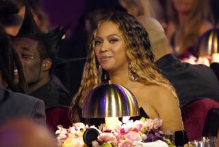 A woman with long brown hair sitting at a table with a lamp and floral bouquet in a crowd