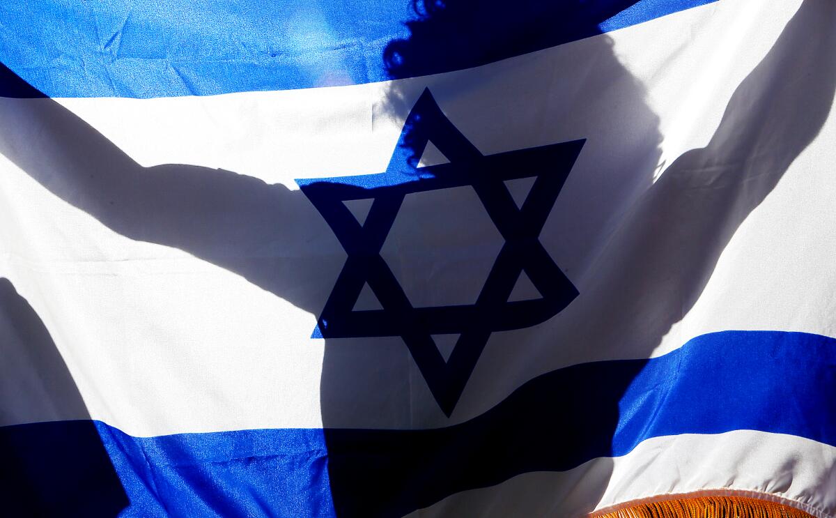 A supporter of Israel is silhouetted in back of an Israeli flag