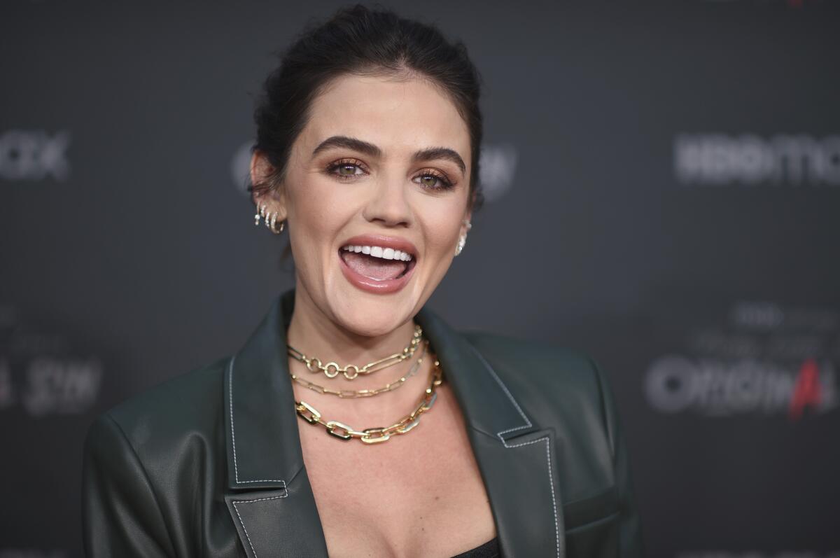 A woman with dark hair smiling with her mouth open, wearing a green leather jacket and gold chain necklaces