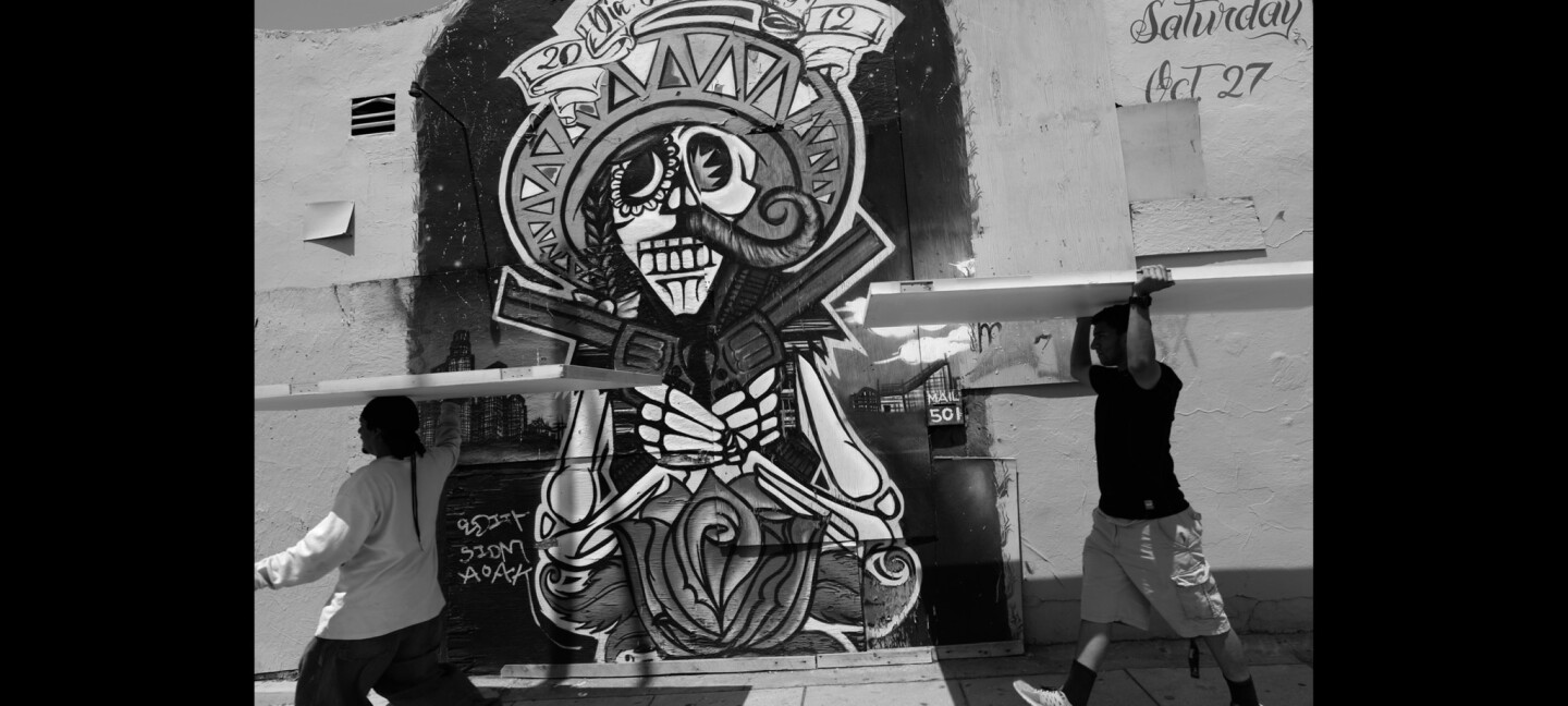 Jesse Jimenez, 39, left, and Eduardo De La Torre, 18, carry doors on their heads as they walk past a Day of the Dead mural in front of the Maravilla Handball Court in East Los Angeles.