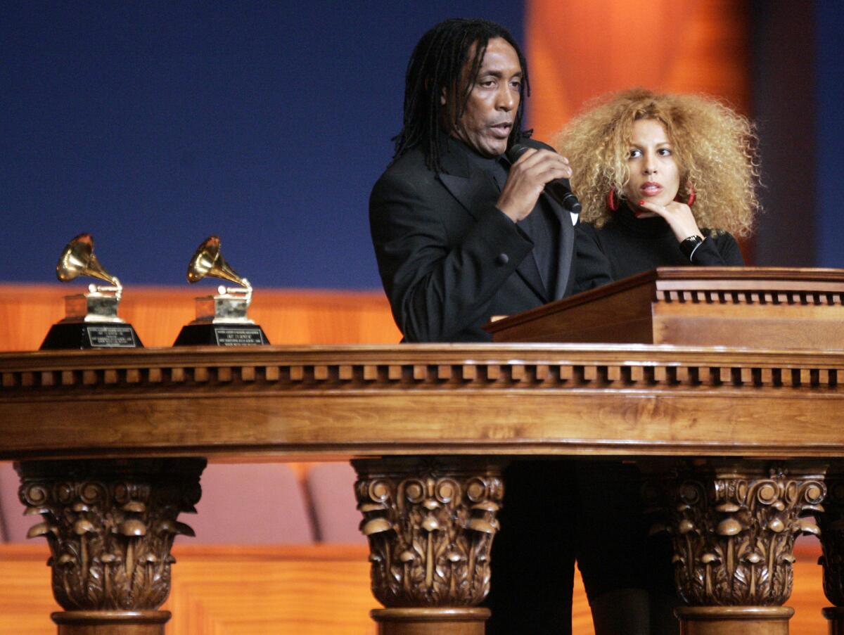 A man dressed in black stands at a wooden lectern and speaks into a microphone next to a woman dressed in black.