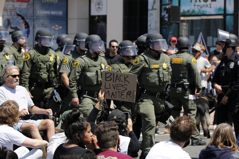 A protester holds up a sign as police shift positions during Saturday's protest in Huntington Beach.